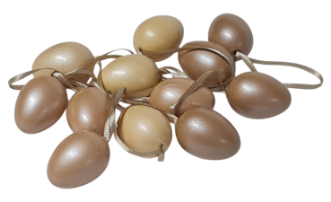 Kleine Ostereier aus Kunststoff in Creme und Beige mit Schlaufe, dekorativ aufgehängt an Frühlingszweigen.