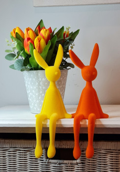 Sitzhase Osterhase in Gelb als Frühlingsdeko auf einem Regal, Beine locker herabhängend