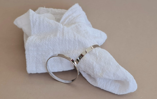 Hochglänzende silberne Serviettenringe auf weißer Tischdecke mit Stoffserviette Hochglänzende silberne Serviettenringe auf weißer Tischdecke mit Stoffserviette